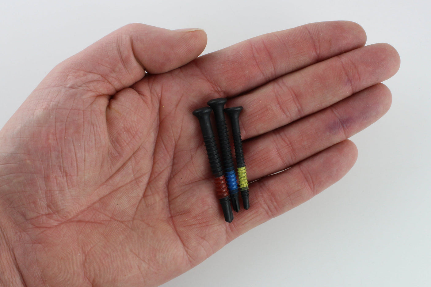 A hand holding three Lokko plug puller screws, one red, one blue, one yellow, showing their small size