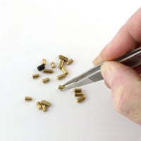 Grooved tweezer tips picking up a brass lock pin from the bench mat