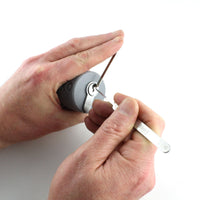 One hand cradling the Lokko support with a euro cylinder inside while the other hand picks the keyway with a tension wrench seated