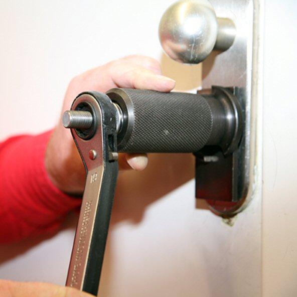 person using a plug puller tool on a door lock with a wrench to remove the cylinder