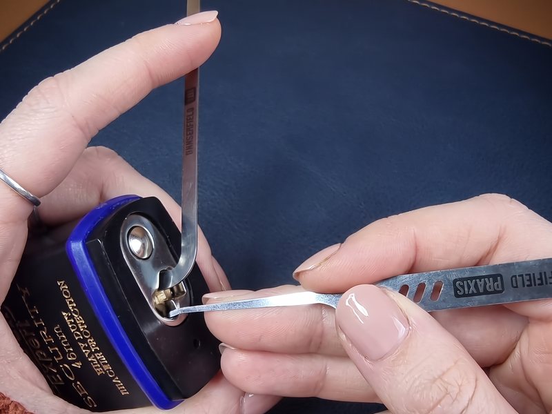 Hands picking a heavy-duty padlock with a Dangerfield PRAXIS hook and tension wrench